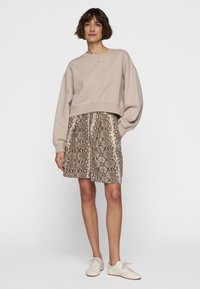 Sudadera corta beige con hombros caídos combinada con una falda hasta la rodilla que presenta un estampado de serpiente en tonos marrón y crema. Zapatillas blancas.