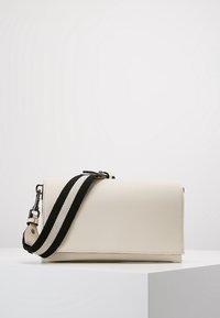 Borsa a tracolla in pelle color crema con pattina, caratterizzata da una tracolla a strisce bianche e nere e dettagli in metallo argentato.