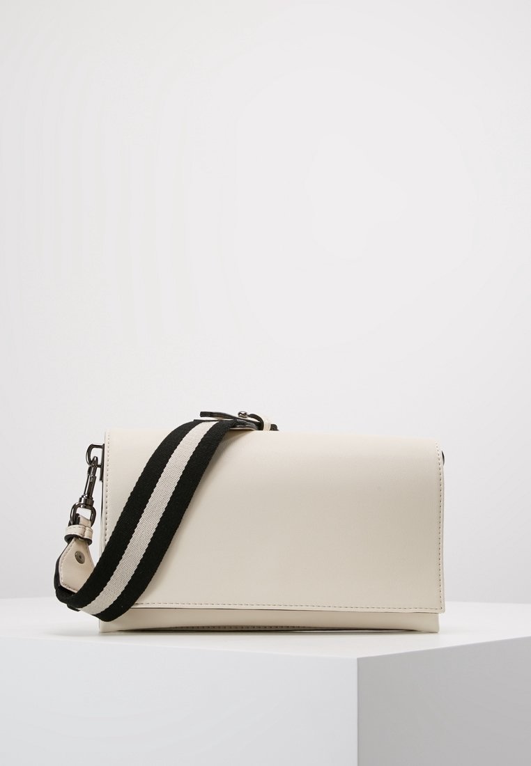 Borsa a tracolla in pelle color crema con pattina, caratterizzata da una tracolla a strisce bianche e nere e dettagli in metallo argentato.