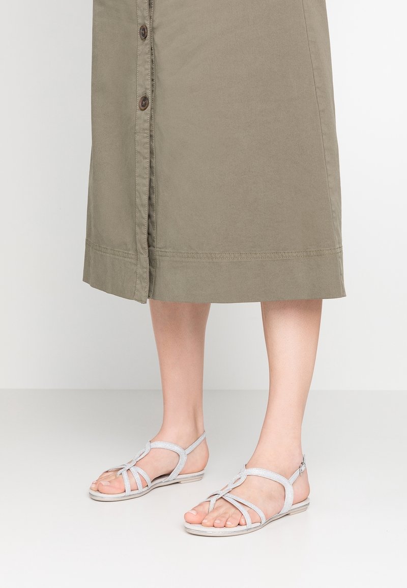 Vaaleanharmaat sandaalit, joissa on useita hihnasuunnitelmia ja matala pohja. Materiaali näyttää pehmeältä ja siinä on teksturoitu pinta.