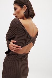 Robe côtelée de couleur brun foncé avec un dos ouvert, des manches longues et un tissu tricoté texturé, mettant en valeur les contours du corps et sa silhouette.