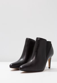 Botines de cuero negro con punta afilada, tacón de aguja delgado y paneles laterales elásticos para un fácil calzado. Textura suave, diseño minimalista.