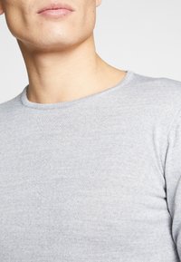 Grå langermet T-skjorte med rund hals, laget av teksturert stoff, viser svak strekk og tettsittende design rundt hals og skuldre.