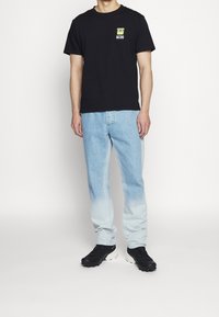 Černé bavlněné tričko s žlutou grafikou, světle modré džíny s gradientním efektem a černé sportovní boty.