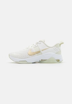 Vita Nike-sneakers med en guldfärgad swoosh. Designen har en texturerad ovandel, vadderad krage och en genomskinlig sula med luftdämpning.