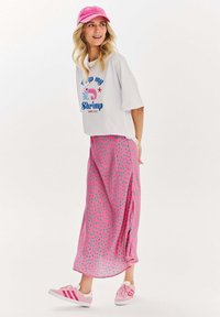 Bílý zkrácený tričko s modrou a růžovou grafikou krevety; růžová maxi sukně s zelenými puntíky; růžová kšiltovka; růžové tenisky s bílými pruhy.