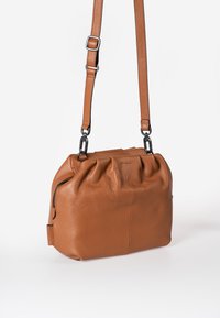 Bruine leren handtas met een geplooid ontwerp, voorzien van een schouderband en ritssluiting. Gladde textuur met een iets gestructureerde vorm.