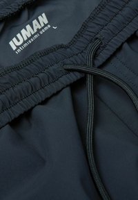 Dunkelblaue Badehose mit elastischem Bund und schwarzem Kordelzug, aus glattem, leichtem Stoff. Das Etikett trägt die Aufschrift "Iuman, intimo uomo, L."