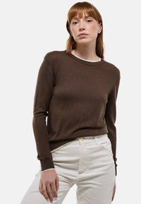 Pull en tricot marron avec un col rond, des manches longues et des poignets côtelés, assorti à un pantalon en velours côtelé blanc. Design simple et classique.