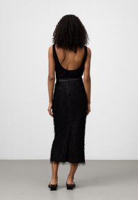Zwarte tanktop met een lage rug, gecombineerd met een zwart mid-length rok met veerachtige textuur en een achterkant split. Soepele, aansluitende pasvorm.
