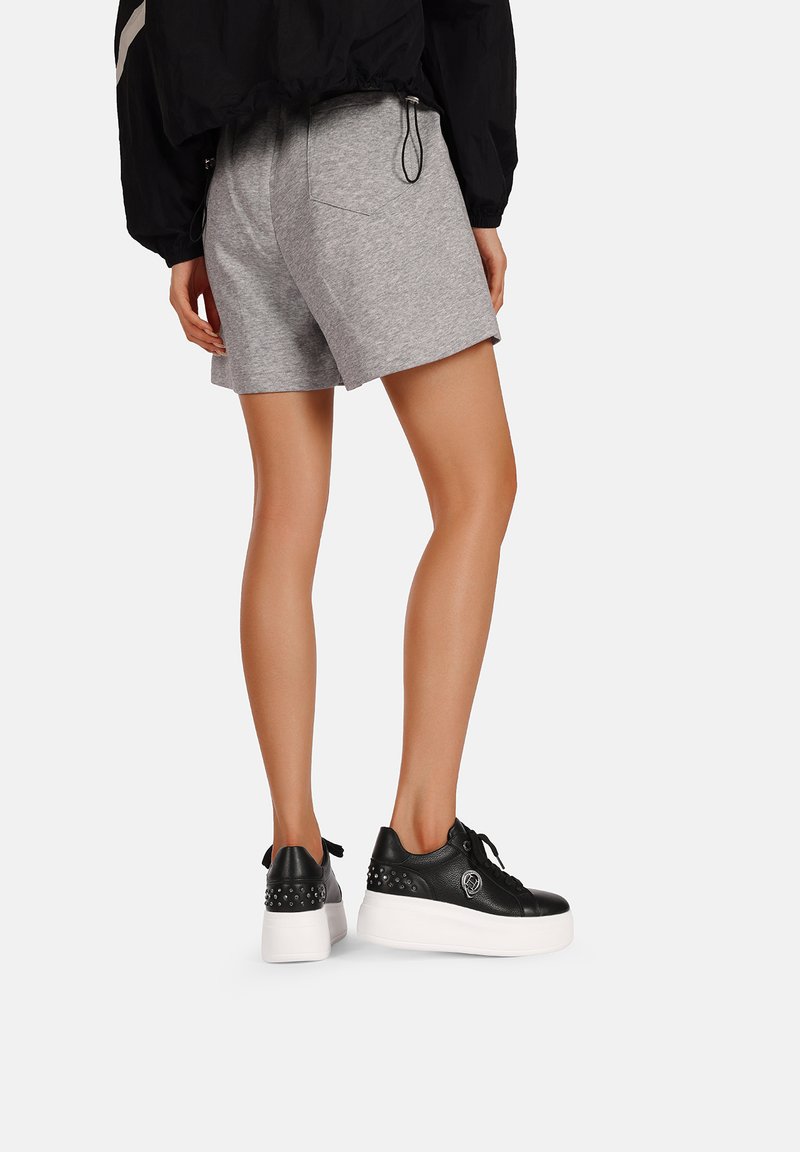 Sneakers platform neri in pelle con suole bianche; presentano borchie silver ai lati; abbinati a pantaloni sportivi grigi.