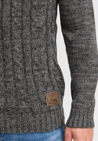 Dark gray knitted sweater featuring a cable knit design, ribbed cuffs, and a textured surface. Includes a small brown brand label at the hem.