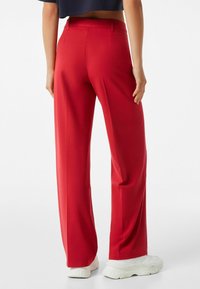 Röda vida byxor i slätt tyg, med hög midja och bakfickor, tillsammans med vita klumpiga sneakers.