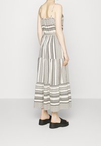 Robe maxi à motifs noir et blanc avec des bretelles fines, design à volants et forme fluide. Portée avec des sandales à plateforme noires.