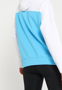 Felpa con cappuccio, parte superiore bianca e pannello inferiore blu; presenta una texture morbida, polsini a costine e una classica tasca a marsupio.