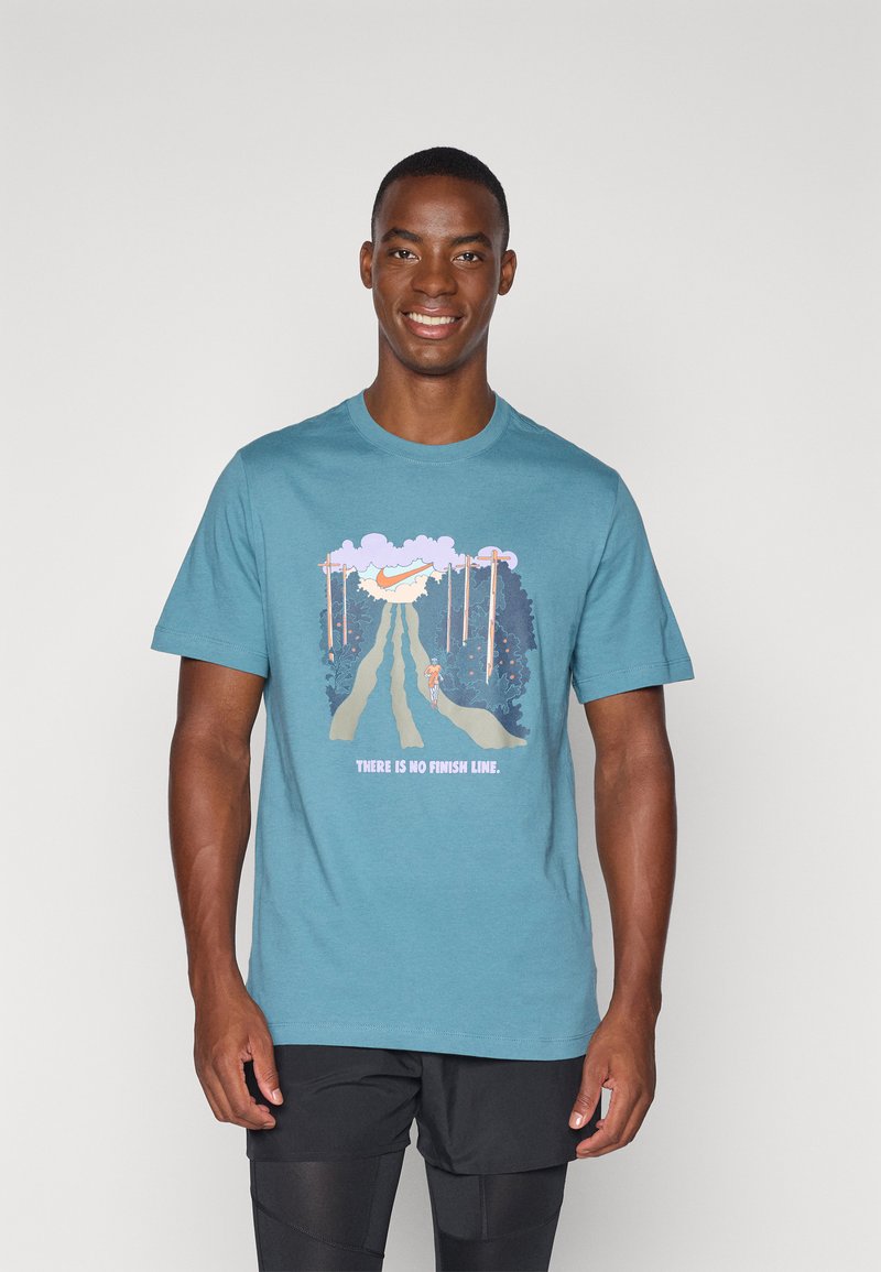 Camiseta de algodón en color azul verdoso con un gráfico de un corredor en un sendero, rodeado de árboles y nubes. El texto dice "No hay línea de meta."