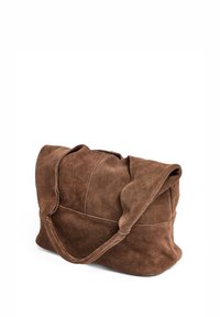 Brown suede tote bag with soft texture, spacious design, curved handles, and a flap closure, featuring visible stitching details.