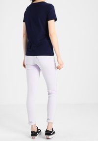 Námořnické tričko s krátkým rukávem spárované se světle fialovými skinny džínami. Džíny mají mírné opotřebení na lemu. Černé tenisky dokonale dotvářejí look.