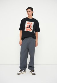 Μ αύρο βαμβακερό μπλούζα με γραφικό "AIR JORDAN" σε κόκκινο και λευκό, συνδυασμένη με φαρδύ γκρι παντελόνι και αθλητικά παπούτσια σε μαύρο, λευκό και γκρι χρώμα.