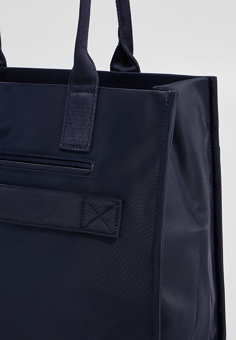Navyfarbene Tragetasche aus robustem Stoff, mit zwei stabilen Griffen, einer mit Reißverschluss versehenen Tasche und einem flachen Boden für Stabilität.