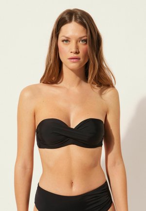 Svart bandeau-bikinitopp med en tvinnad design fram, slät textur och inga axelremmar. Matchas med svarta höga bikinitrosor.
