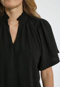 Blusa nera con scollatura a V e colletto arricciato. Maniche corte a sbuffo e tessuto morbido e testurizzato. Design semplice senza motivi o decorazioni.