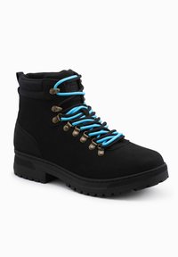 La bota de senderismo negra de ante presenta cordones azules, ojales metálicos y una suela de goma texturizada para un buen agarre. Altura hasta el tobillo con cuello acolchado.