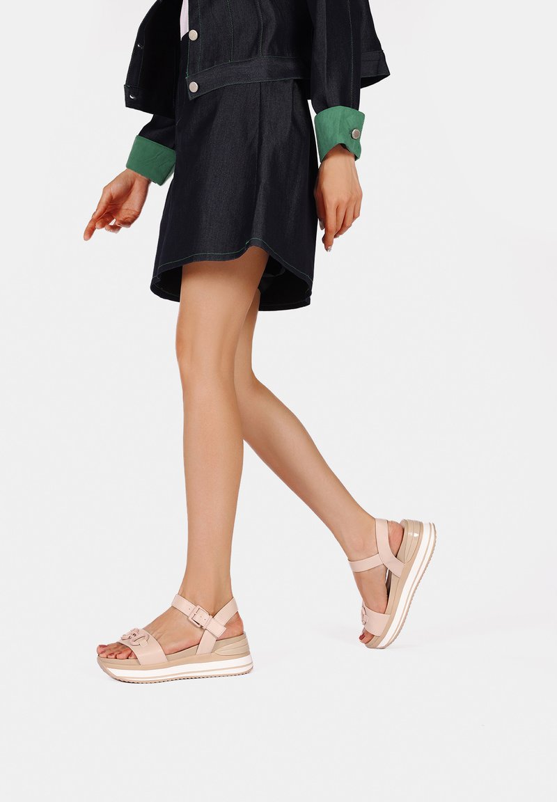 Sandali platform rosa chiaro con design a più cinghie, dotati di fibbia regolabile alla caviglia e suola testurizzata rialzata, indossati con un vestito di jeans.