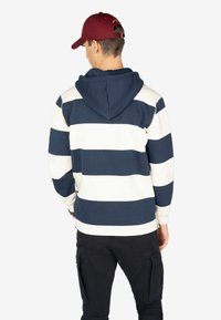 Sudadera a rayas en azul marino y blanco con un bolsillo tipo canguro y capucha ajustable; combinada con pantalones cargo negros con bolsillos laterales.