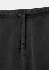 Pantaloni sportivi neri realizzati in un tessuto di cotone texturizzato, con una vita elastica dotata di cordoncino e una tasca laterale.