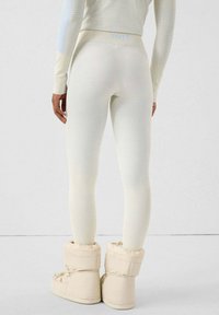 Leggings de color claro con textura acanalada y cintura alta. Combinados con botas acolchadas de tobillo de color crema.