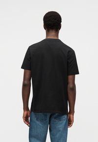 Μαύρο κοντομάνικο T-shirt με λαιμόκοψη, κατασκευασμένο από βαμβάκι. Διαθέτει άνετη εφαρμογή και λεία υφή, φορεμένο με μπλε τζιν παντελόνι.