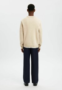 Beige stickad tröja med rund hals och ribbade muddkragar, kombinerad med mörkblå vida byxor. Synlig textur i tröjans tyg.