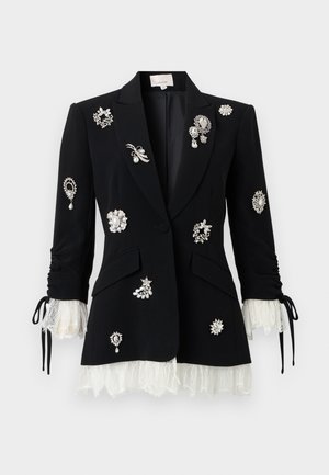 Black tailored blazer with white lace cuffs and hem, adorned with various silver and pearl decorative brooches on front and sleeves.