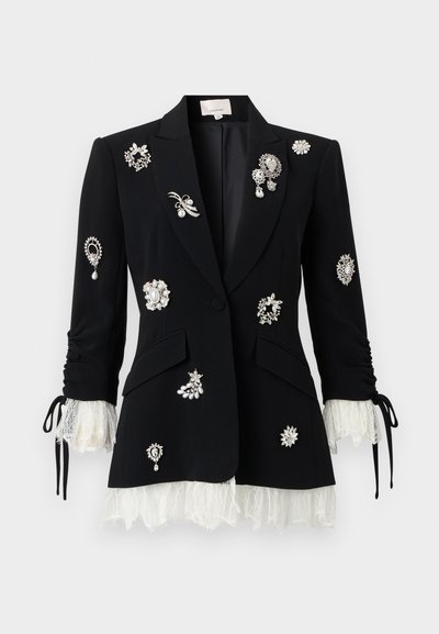 Μαύρο ραμμένο σακάκι με λευκές δαντελένιες μανσέτες και τελείωμα, διακοσμημένο με διάφορα ασημένια και μαργαριταρένια διακοσμητικά καρφίτσες στο μπροστινό μέρος και στα μανίκια.
