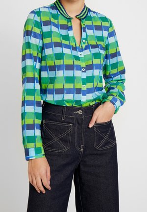 Overhemd met knopen in groen-blauw geometrisch patroon, met kraag, lange mouwen met knoopmansetten, gecombineerd met een donkere spijkerbroek.