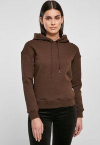 Sudadera con capucha marrón, con cordones, puños y dobladillo acanalados. Textura suave, corte relajado y una pequeña etiqueta de marca en el costado.