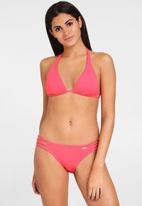 Bikini rosa con un top triangular y tirantes halter, y un fondo con múltiples tirantes laterales. El material parece suave y elástico.