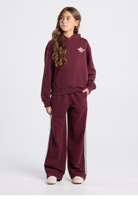 Viininpunainen huppari etutaskulla, yhdistetty yhteensopiviin viininpunaisiin verkkarihousuihin, joissa on valkoiset sivuraidat. Pehmeä kangas, rento istuvuus.