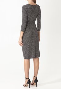 Czarna i biała sukienka w wzory z rękawami o długości trzech ćwierć, dopasowana sylwetka, długość do kolan, zestawiona z czarnymi sandałami na wysokim obcasie.