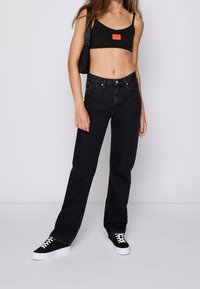 Svarta högmidjade jeans med rak benkjol, fem fickor och subtila röda sömmar. Kombineras med en svart kort topp och svarta sneakers.