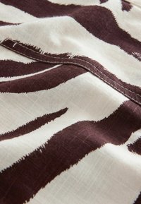 Tissu en coton présentant un motif audacieux de rayures de zèbre en brun foncé sur un fond crème, avec une texture visible et des détails de couture.