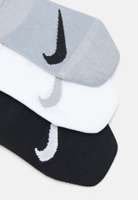 Tre par sokker: lysegrå, hvite og svarte. Hver har et Nike-logo i kontrasterende farger. Materialet ser ut til å være strikket med en strukturert overflate.