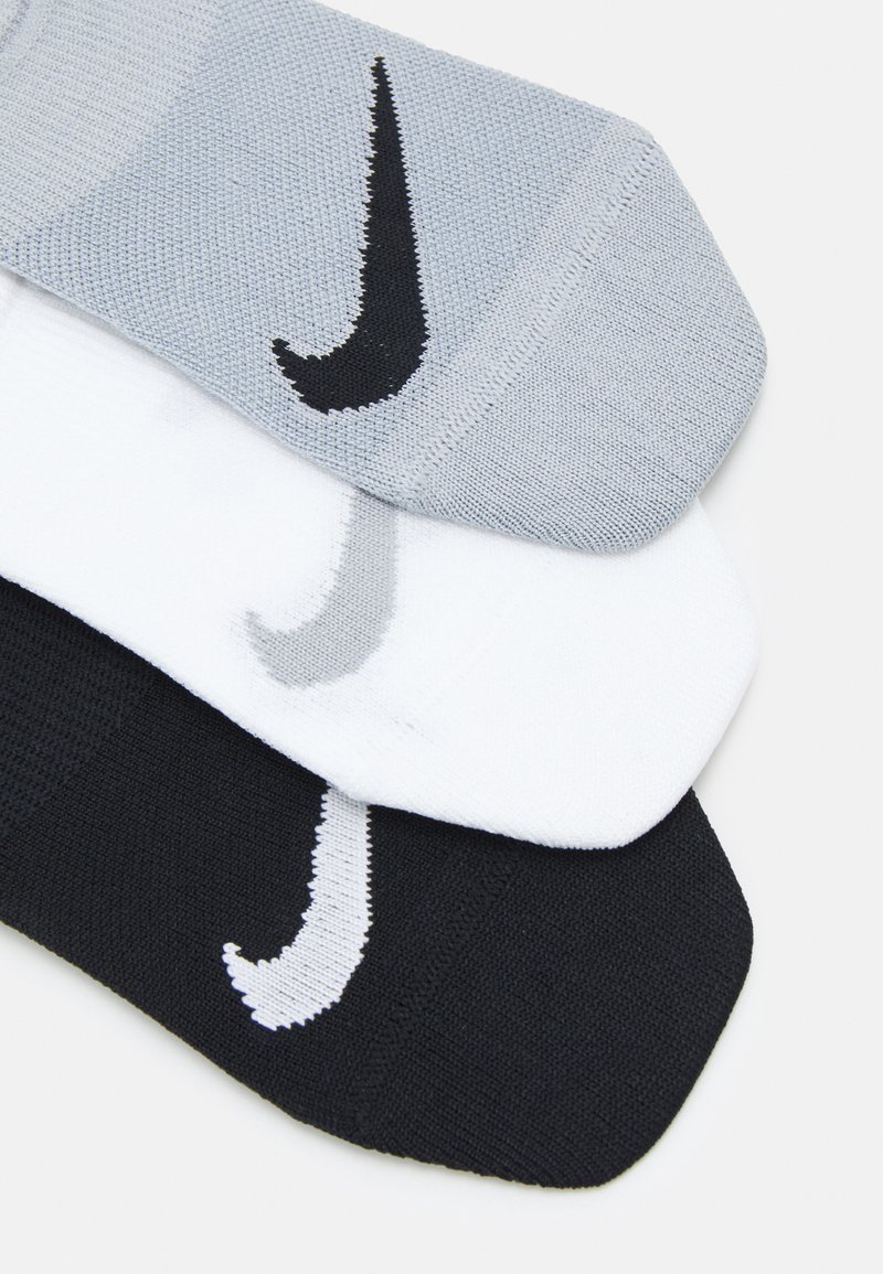 Tre par sokker: lys grå, hvid og sort. Hver har et Nike-logo i kontrastfarver. Materialet ser ud til at være strikket med en tekstureret finish.