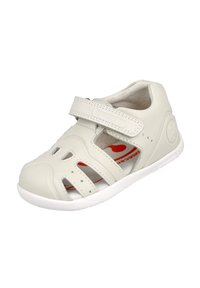 Sándalo de cuero blanco con diseño troquelado y correa de velcro. Cuenta con una plantilla acolchada y una suela flexible de goma blanca.