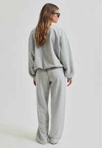 Sudadera gris y pantalones de pierna ancha hechos de un tejido suave. La sudadera tiene hombros caídos, mientras que los pantalones cuentan con una cintura elástica.