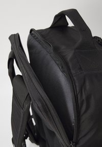 Sac à dos noir avec compartiment rembourré pour ordinateur portable ouvert, avec fermeture éclair et poignée de transport solide sur un fond clair.