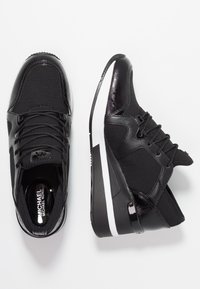 Chaussures de sport noires en mesh texturé mélangé à des matériaux synthétiques lisses. Elles présentent une semelle blanche, un système de lacets et des détails d'accentuation.