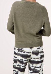 Maglione a maglia verde oliva con orlo a coste e maniche raglan, abbinato a pantaloni neri e bianchi a fantasia con un design simile a nuvole.