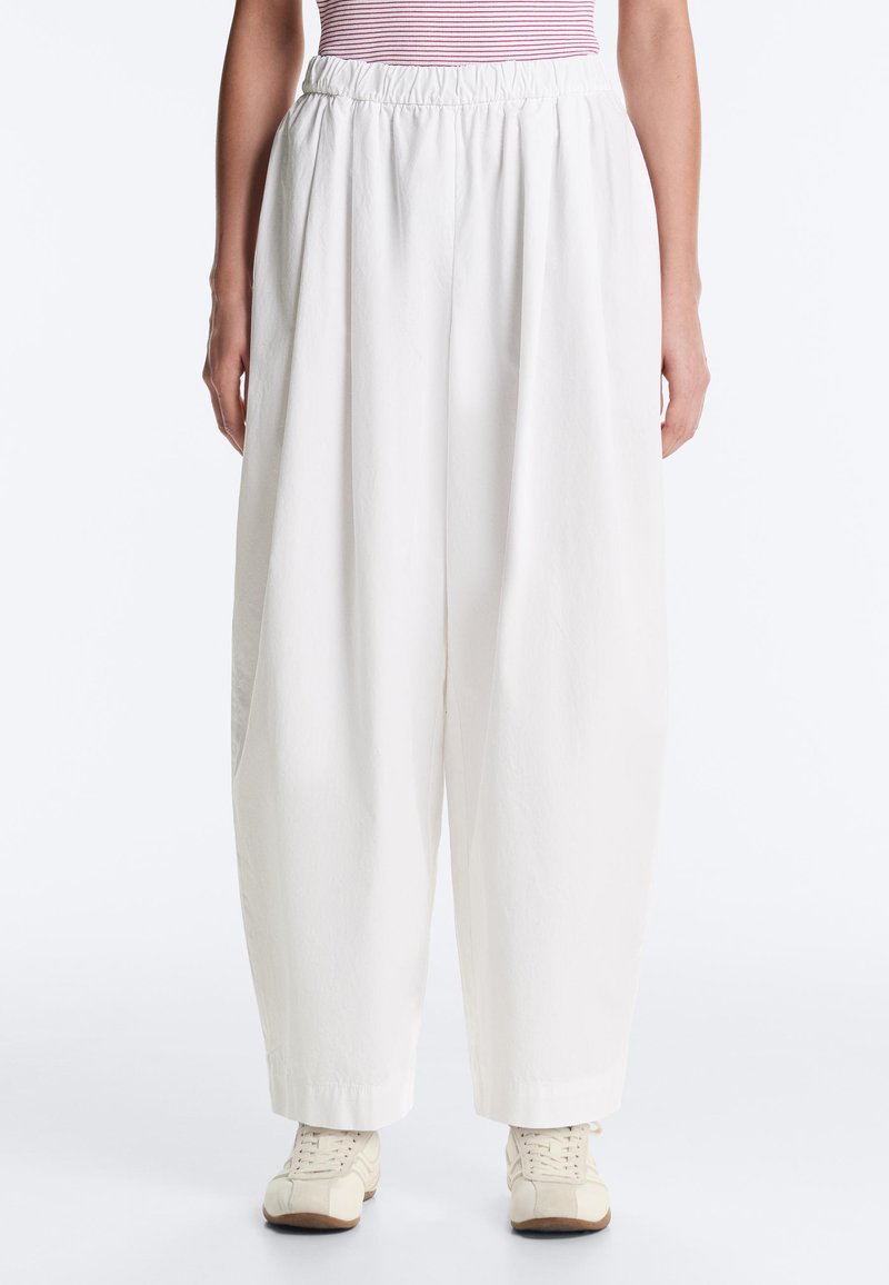 Femme portant un pantalon blanc ample avec une ceinture élastique, associé à des baskets blanches et un haut rayé rose.